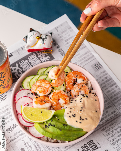 Bowl with shrimps, cucumbers, radishes, avocado, sesame seeds and auce on the background of a Japanese newspaper photo