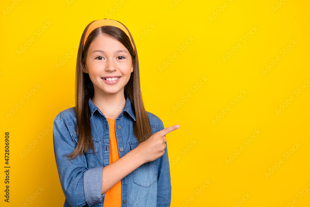 Photo of adorable shiny student girl wear denim shirt smiling pointing finger empty space isolated yellow color background Photo of adorable shiny student girl wear denim shirt smiling pointing finger empty space isolated yellow color background