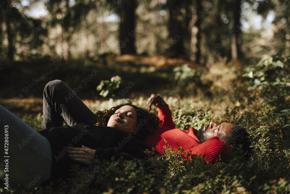Pregnant woman relaxing while lying with boyfriend on plants in forest Pregnant woman relaxing while lying with boyfriend on plants in forest