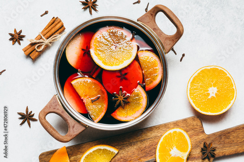 Hot Mulled wine cooking at home for happy christmas time. Red wine, orange, apple and spices - ingredients boiling in a pot on white table background. Warming new year and holiday drink, flat lay.