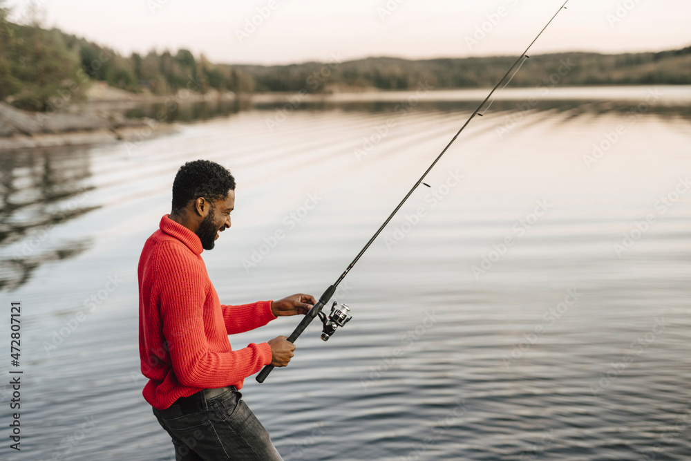 Smiling man fishing in lake during sunset Smiling man fishing in lake during sunset