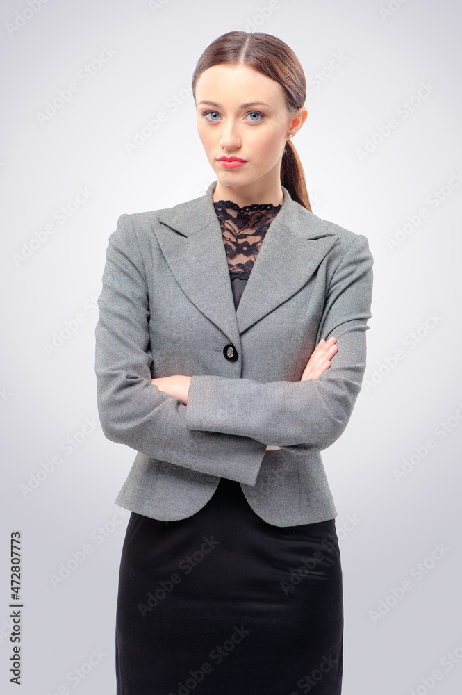 Confident beauty. Beautiful young business woman looking at camera and keeping arms crossed while standing isolated on grey.