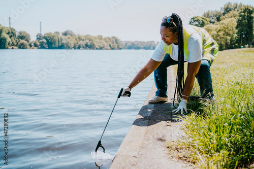 Mature female volunteer cleaning plastic with claw from lake photo
