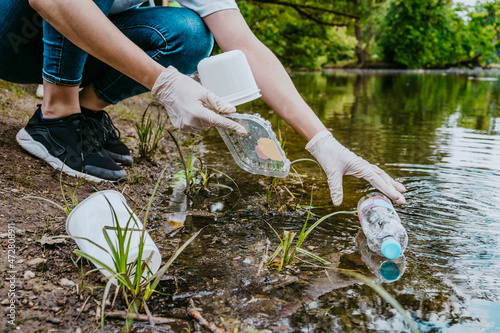 Low section of female volunteer cleaning plastic waste from pond at park photo