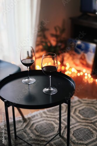 Two glasses of red wine on a black table in a living room  garland lights on the background  Christmas winter mood