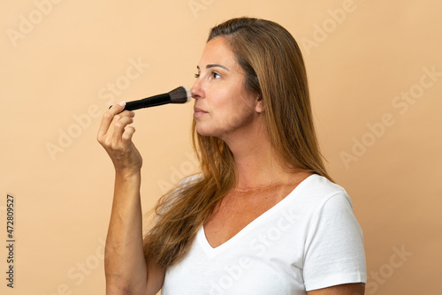 Middle age brazilian woman isolated on beige background holding makeup brush