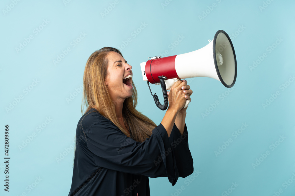 Middle age brazilian woman isolated on blue background shouting through a megaphone Middle age brazilian woman isolated on blue background shouting through a megaphone