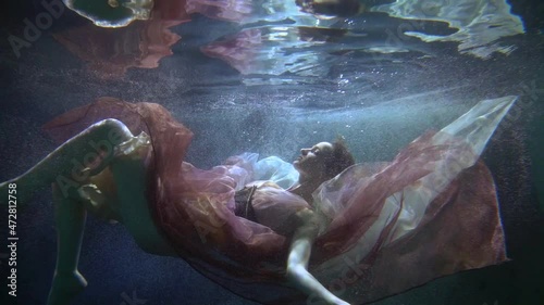 A beautiful woman elegantly floating underwater in a dress like a mermaid in a fairy tale photo