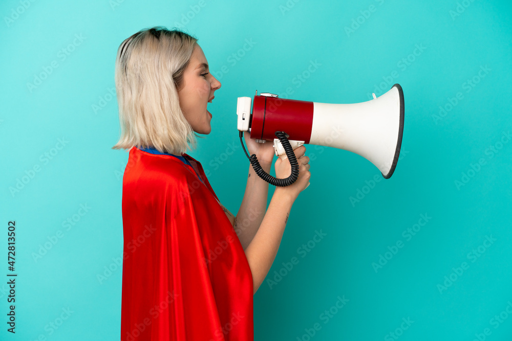 Super Hero caucasian woman isolated on blue background shouting through a megaphone Super Hero caucasian woman isolated on blue background shouting through a megaphone