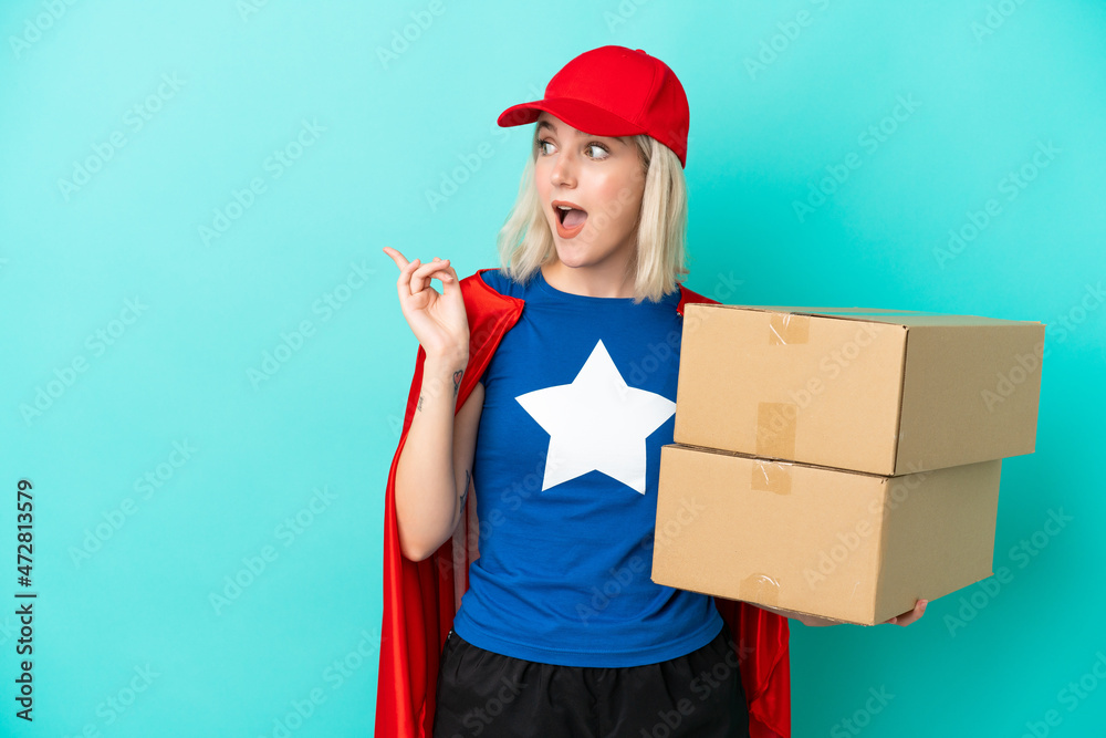 Super Hero caucasian delivery woman isolated on blue background intending to realizes the solution while lifting a finger up Super Hero caucasian delivery woman isolated on blue background intending to realizes the solution while lifting a finger up