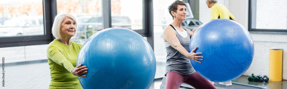 Grey haired sportswoman holding fitness ball in sports center, banner. Grey haired sportswoman holding fitness ball in sports center, banner.