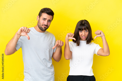Young couple isolated on yellow background showing thumb down with both hands