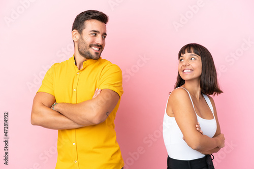 Young couple isolated on pink background looking over the shoulder with a smile