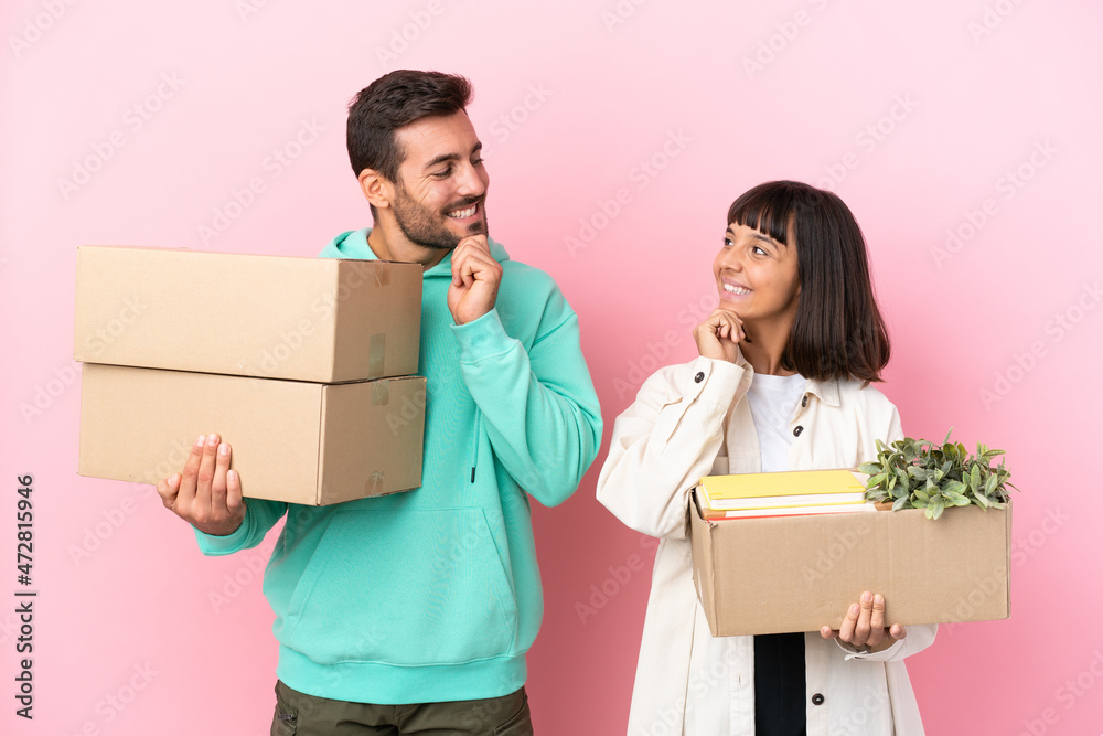 young beauty couple moving in new home among boxes isolated on pink background looking looking at each other young beauty couple moving in new home among boxes isolated on pink background looking looking at each other