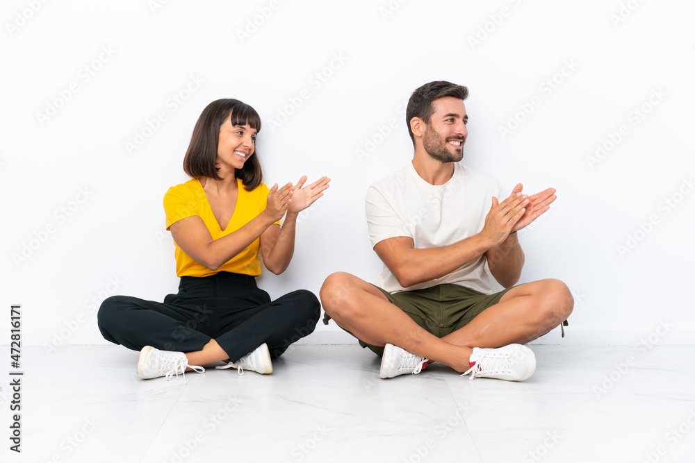 Young couple sitting on the floor isolated on white background applauding after presentation in a conference Young couple sitting on the floor isolated on white background applauding after presentation in a conference