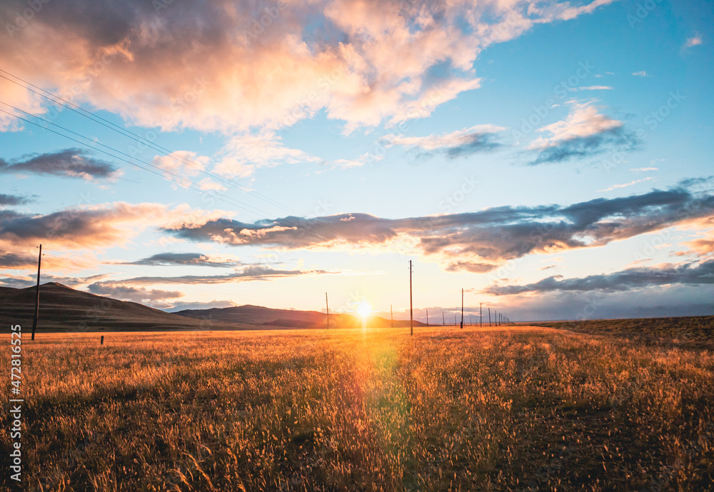 Stunning rural landscape. Sunset over the golden wheat field. Blue sky with dramatic clouds at sunset. Sun sets down. Summer. Stunning rural landscape. Sunset over the golden wheat field. Blue sky with dramatic clouds at sunset. Sun sets down. Summer.