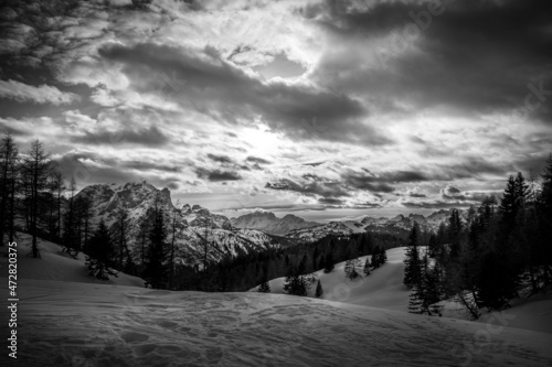 Black and white winter panorama of Mount Civetta with dolomite peaks background and the sun peeking through the clouds. Fiorentina Valley, Dolomites, Italy