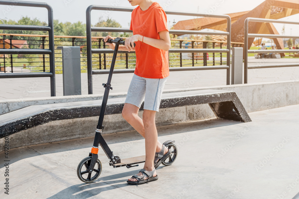 A young teenage boy rides a scooter in a city skatepark. Safety and trending transport for youth A young teenage boy rides a scooter in a city skatepark. Safety and trending transport for youth