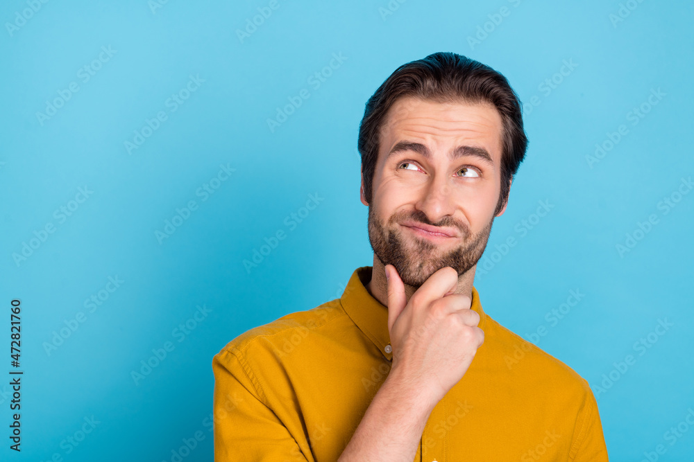 Photo of thinking millennial brunet guy look empty space wear yellow shirt isolated on blue color background Photo of thinking millennial brunet guy look empty space wear yellow shirt isolated on blue color background