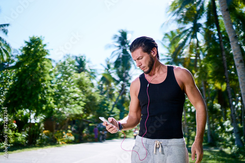 Sport and technology. Young strong man listening music with earphones and smartphone outdoors.