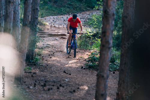 Fit cyclist riding his bike downhill through a forest ( woods ) while wearing a red shirt and red shoes.