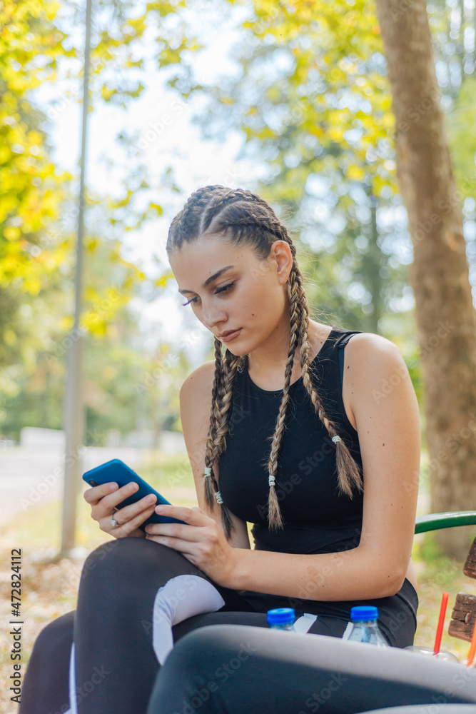 Hot attractive women smiling and swiping on their phones while sitting in a park and taking a break from their sports activities. Hot attractive women smiling and swiping on their phones while sitting in a park and taking a break from their sports activities.