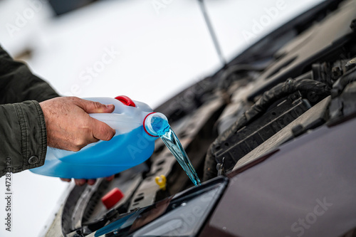 driver refilling the blue non-freezing windshield washer liquid in the tank of the car, close-up photo