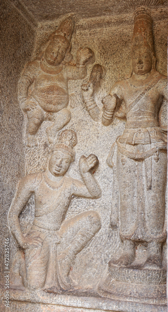 Statue of a Hindu god carved in stone. The rock is located in the background