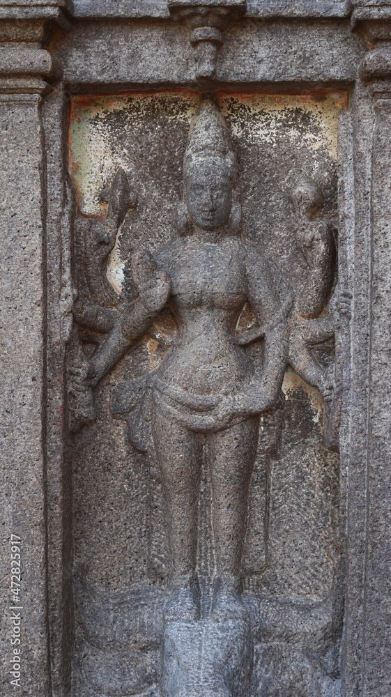 Statue of a Hindu god carved in stone. The rock is located in the background