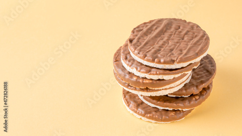 Stack of round rice cakes covered with dark chocolate on yellow background. Healthy Gluten Free cereal crispbread.
