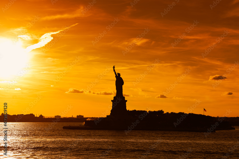 Naklejka premium Travel to Manhattan, visit New York. Amazing summer sunset over Statue of Liberty with spectacular dramatic sky. One of the most known landmark in United States.