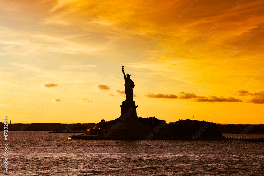 Travel to Manhattan, visit New York. Amazing summer sunset over Statue of Liberty with spectacular dramatic sky. One of the most known landmark in United States.