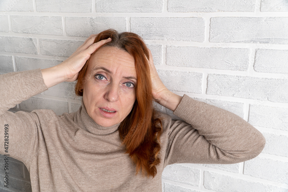 Portrait of a man on a background of a gray brick wall. An adult woman clutched her head in a fit of stressful experiences. Negative emotion concept. Portrait of a man on a background of a gray brick wall. An adult woman clutched her head in a fit of stressful experiences. Negative emotion concept.