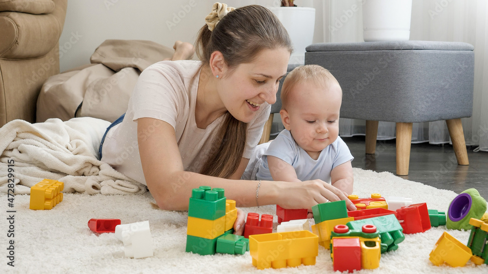 Happy smiling mother with baby son building toy tower with colorful bricks and blocks. Concept of children development, education and creativity at home Happy smiling mother with baby son building toy tower with colorful bricks and blocks. Concept of children development, education and creativity at home