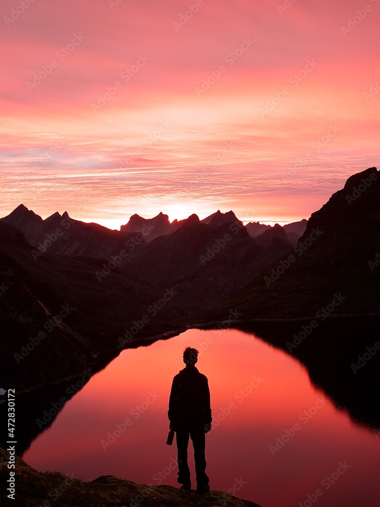 silhouette of a person standing on a mountain scouting the water at sunset. Captured in the Lofoten Islands in Norway