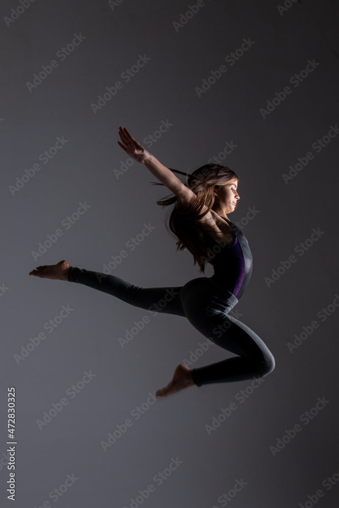 young woman doing artistic gymnastics jumps, wearing gym clothes, photo taken in a studio.