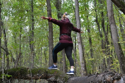 The girl walks along a fallen tree in the forest.