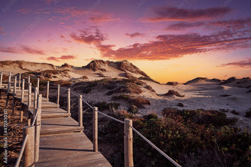 Wooden pedestrian walkway through natural park with beautiful sunset sky. Wild sandy landscape, with part of Cresmina Dunes. Beautiful scenery in Portugal.