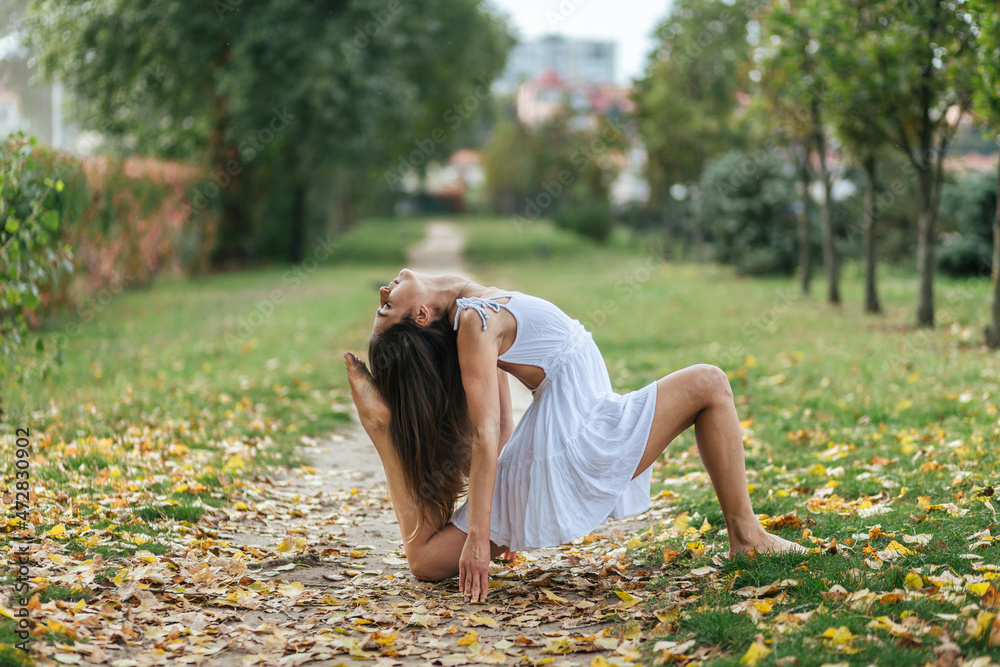 Obraz premium beautiful girl in white dress doing yoga poses in the autumn park, balance, fitness, stretching and relaxation