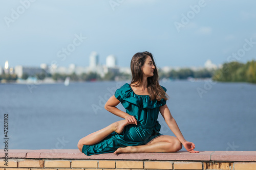beautiful girl in green dress doing yoga poses in the autumn park near the river, balance, fitness, stretching and relaxation