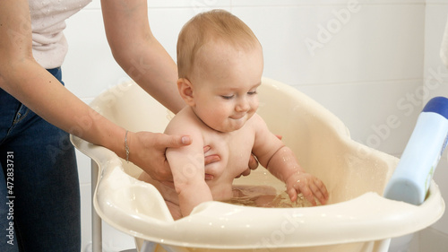 Cheerful smiling baby boy splashing water and playing while having bath with mother. Concept of children hygiene, healthcare and parenting.