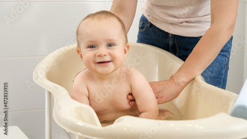 Adorable smiling baby boy looking in camera while sitting in bath at bathroom