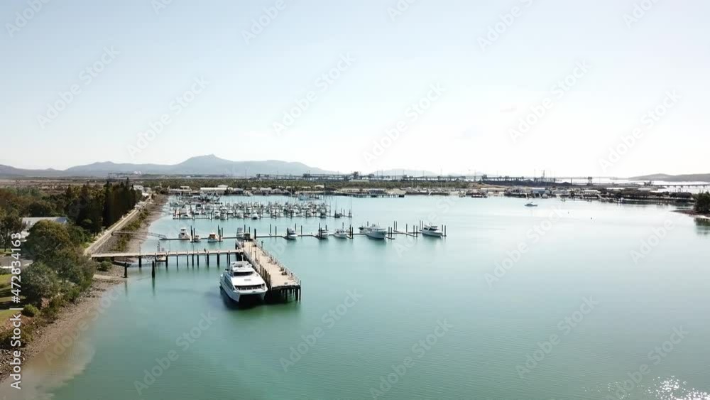 Drone aerial slow pan over blue water harbour on a sunny day with a park