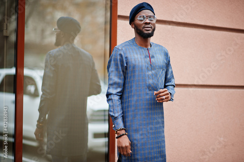 African guy in blue authentic costume, eyeglasses and beret. Fashionable nigerian man.