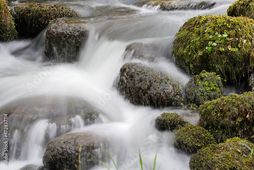 Traumhafter Fluss oder Bach mit sanft fließendem Wasser, welches in Kaskaden über runde mit Moss bewachsene Steine herab fällt
