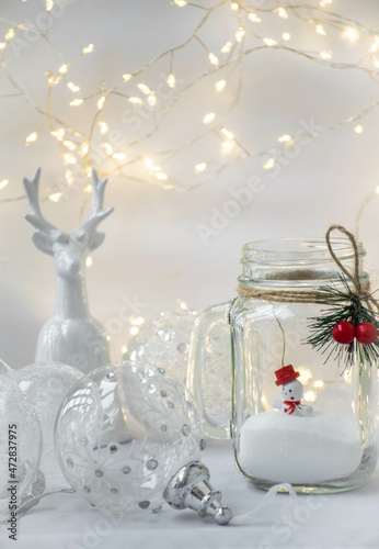 Moscow, Russia, December 2021, Christmas card, background, decorative jar with a snowman inside, Christmas balls, a figurine of a deer and a garland of lights on a white background