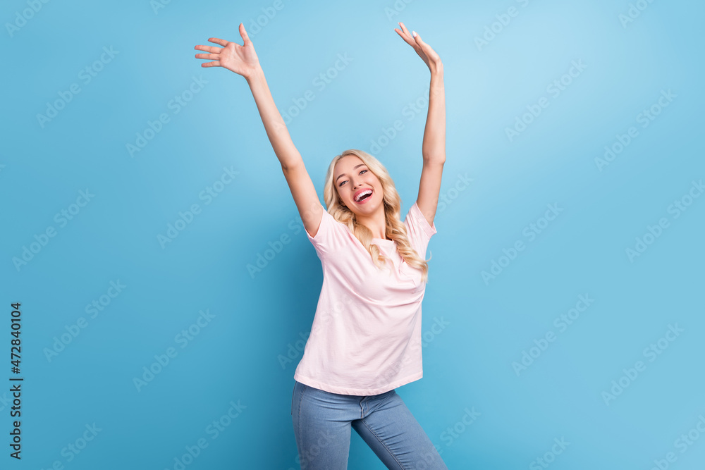 Photo of funky young blond lady dance wear pink t-shirt jeans isolated on blue color background Photo of funky young blond lady dance wear pink t-shirt jeans isolated on blue color background