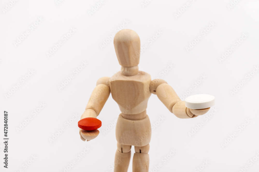 A wooden Gestalta doll or mannequin holds red and white pills in its hands on light background. The concept of choice. A wooden Gestalta doll or mannequin holds red and white pills in its hands on light background. The concept of choice.