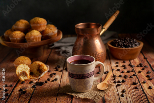 cup of coffee with traditional copper coffee pot with wooden bowl with fresh coffee beans and muffins on wooden table