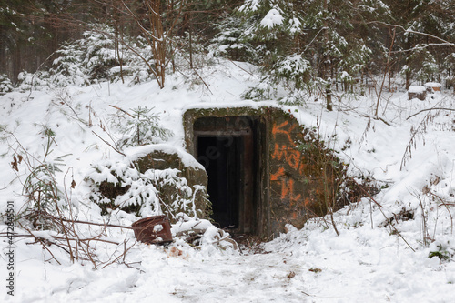 An abandoned, destroyed concrete bunker with an embrasure in a winter forest. Bunker entrance. photo